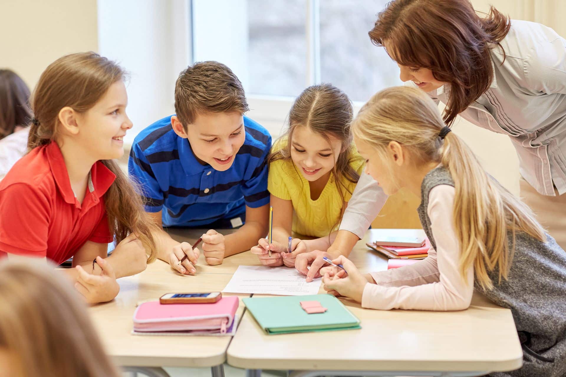 Gruppo di quattro studenti, che svolgono insieme un'attivit&agrave; di classe, affiancati da un'insegnante