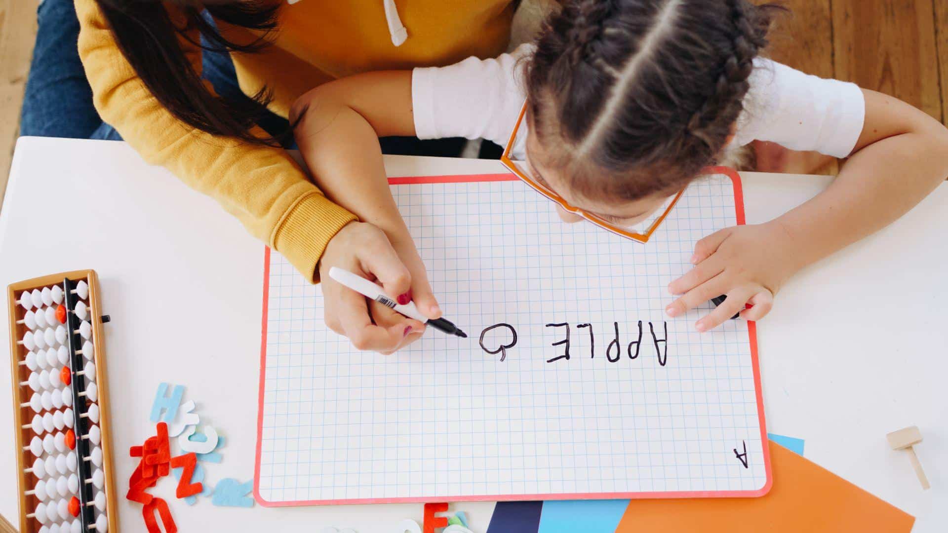Insegnante aiuta una bambina a scrivere su una piccola lavagna